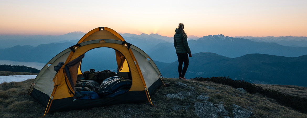 Woman standing on a cliff overlooking a sunset next to her tent.