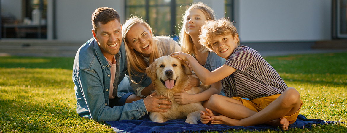 A family with two children petting their smiling golden retriever.